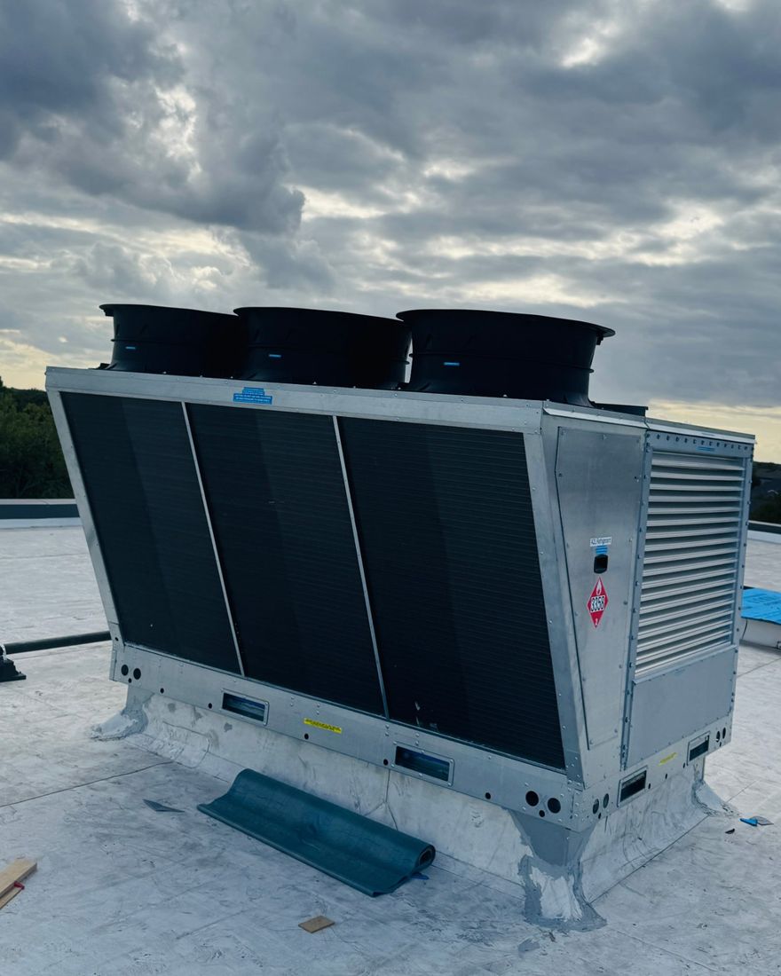 A new rooftop outdoor-air unit set on its curb on a North Texas commercial roof under a cloudy sky